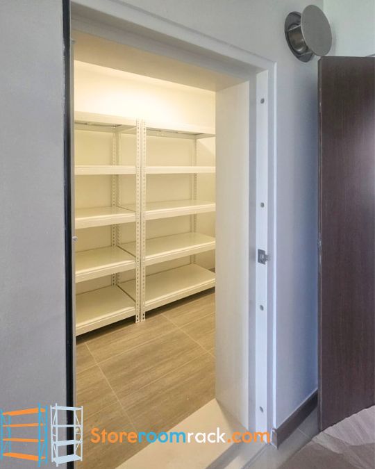 Beige boltless shelving installed inside a BTO household shelter, seen through the open shelter door, with four shelf levels and the lowest shelf raised clear of the tiled floor